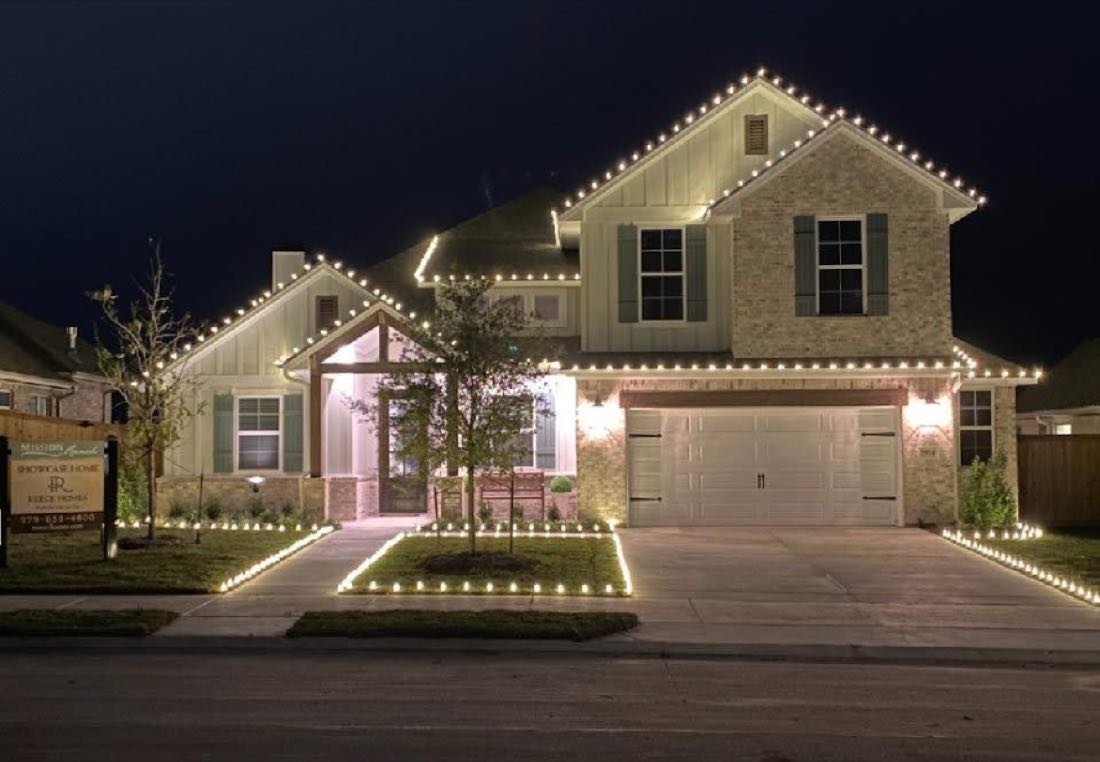 Two-story home with lit rooflines and ground stake lights outlining the front walkway and garden beds.